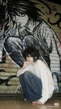 a young man sitting on the ground in front of a graffiti wall with his hands under his chin