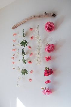 pink and white flowers are hanging on the wall next to a driftwood branch with branches