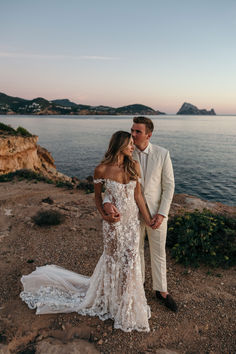 a man and woman standing next to each other in front of the ocean at sunset