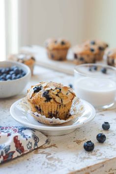 blueberry muffins on a white plate next to some yogurt and milk