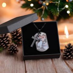 a christmas ornament in a gift box with a candle and pine cones behind it