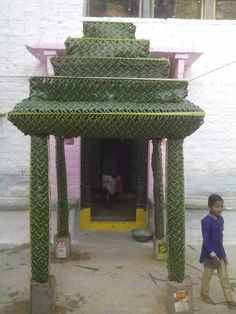 a little boy standing in front of a building with green pillars and columns on each side