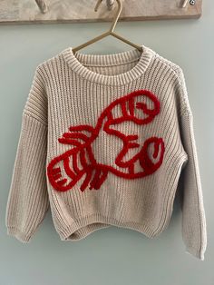 a white sweater with red letters on it hanging from a coat hook in front of a blue wall