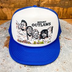 This exclusive trucker hat design from BiggieTexas features the "Mount Rushmore of Outlaw Country music": Willie Nelson, Waylon Jennings, Kris Kristofferson, and Johnny Cash.  This hat fits slightly smaller than our regular trucker hats. These adjustable snapbacks size up and down to fit most small to regular size adults, as well as youths. * Size: Small Adult / Youth * Crown height: 3-1/2", or Mid-Crown * Hat type: Structured * Snap type: Plastic * Trim: Braided Rope * Brim style: Curved This d Fan Merchandise Snapback Trucker Hat, Adjustable Flat Bill Trucker Hat For Fan Gear, Flat Brim Trucker Hat For Fan Gear, One Size Flat Bill Trucker Hat For Fan Gear, Graphic Print 5-panel Hat One Size, Graphic Print 5-panel Hat, Adjustable Outdoor Hat With Graphic Print, Graphic Print Snapback Hats For Outdoor, Adjustable 5-panel Hat With Graphic Print