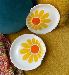 two yellow and white plates sitting on top of a chair next to a blue pillow