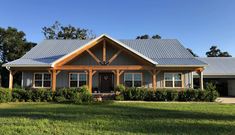 a house that is in the grass with a blue roof and some bushes around it