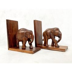 two wooden elephants standing next to each other on top of a white surface with one elephant facing the opposite direction