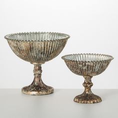 two silver glass bowls sitting on top of a white table next to eachother