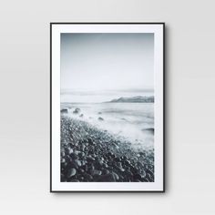 a black and white photo hanging on a wall above a beach with rocks in the foreground