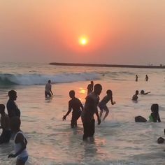 many people are playing in the water at sunset