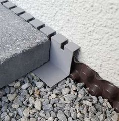 the corner of a building that has some rocks and gravel around it, with a concrete block on top