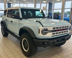 a light blue truck is parked in a showroom with large windows and tile flooring