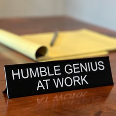 a sign that says humble genius at work sitting on a table next to a notebook