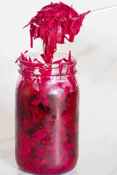 a jar filled with red flowers on top of a white countertop next to a wooden spoon