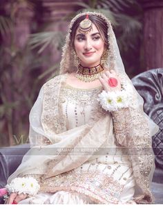 a woman in a white dress sitting on a bench wearing a tiara and holding flowers