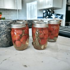 four jars filled with tomatoes sitting on top of a counter