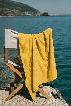 a yellow towel sitting on top of a wooden chair next to the ocean with mountains in the background