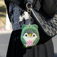 a person wearing a black dress holding a green and white owl keychain with a pink rose in it's mouth