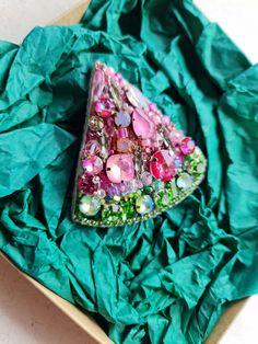 a triangle shaped brooch sitting on top of a green piece of paper in a box