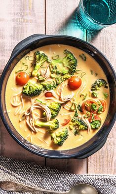 a bowl of soup with broccoli, tomatoes and noodles in it next to a glass of water