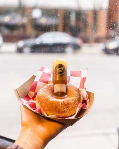 a person holding a donut with a bottle on top of it in front of a window