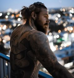 a man with tattoos on his back looks out over the city at night from a balcony