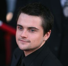 a close up of a person wearing a black suit and diamond earring on the red carpet