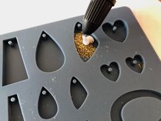 a person is using a drill to make heart shaped holes in a cookie sheet with gold glitter