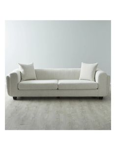 a white couch sitting on top of a hard wood floor next to a gray wall