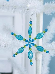 a snowflake ornament hanging from a white christmas tree with blue and green beads