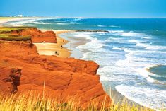 the beach is lined with red rocks and grass, while people are walking on the shore