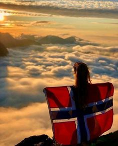 a woman sitting on top of a mountain with a flag in her lap looking out over the clouds