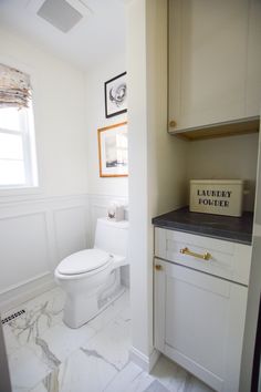 a white toilet sitting inside of a bathroom next to a sink and window with pictures on the wall