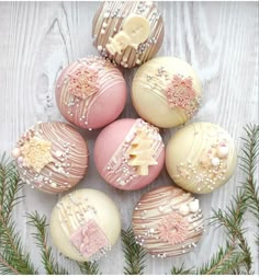 some decorated chocolates are sitting on a white wooden surface with pine branches around them