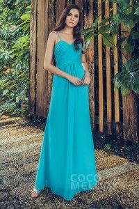 a woman standing in front of a wooden fence wearing a long blue dress with straps