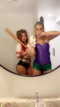 two women in costumes are taking a selfie with their cell phones and holding baseball bats