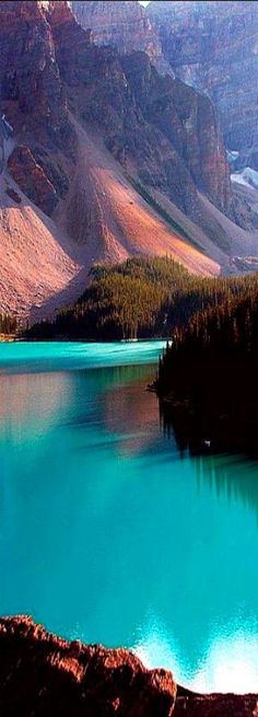 a lake surrounded by mountains and trees in the middle of it's blue waters