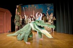 an alligator is on stage with people in the background and one person holding up his arms