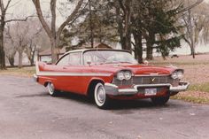 an old red and white car parked on the side of the road in front of some trees