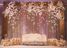 a couch sitting under a flower filled canopy in front of a stage with flowers hanging from the ceiling