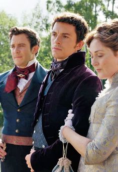 two men and a woman standing next to each other in period clothing, with trees in the background