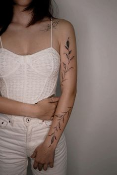 a woman with tattoos on her arms and chest standing in front of a white wall