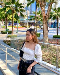 a woman is standing on the steps in front of some palm trees and looking off into the distance