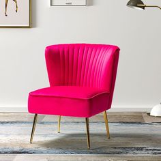 a pink chair sitting on top of a wooden floor next to a lamp and pictures