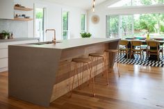 a kitchen with an island and bar stools next to it, in front of large windows