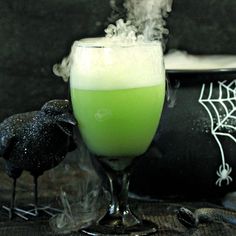 a green liquid in a glass next to a black candle and some spooky decorations