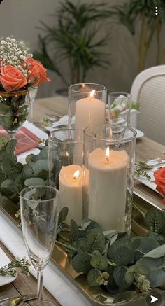 candles are lit on a table with flowers and greenery