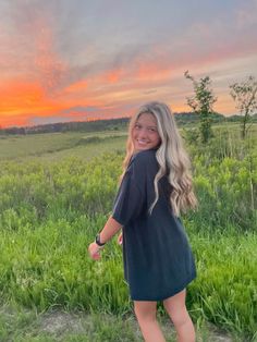 a woman is standing in the grass at sunset