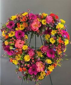 a floral wreath on a stand with flowers in the shape of a heart, placed against a gray background