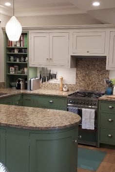 a large kitchen with green cabinets and marble counter tops on the island in front of the stove